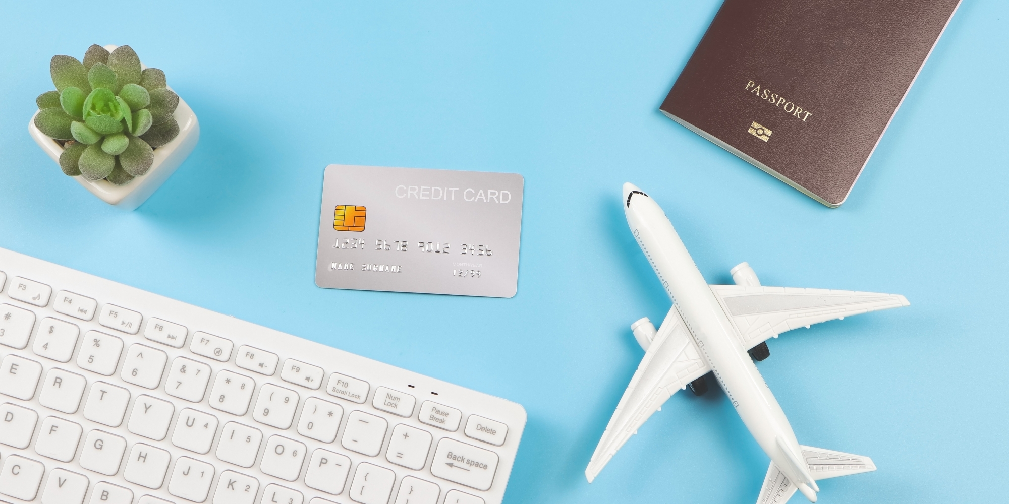A credit card next to a toy airplane, passport, keyboard and mini succulent.